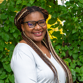 Portrait of CoED Faye Macheke smiling and standing in front of greenery