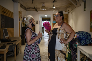 Photo of two women talking to each other, one of them is holding a handheld fan. 