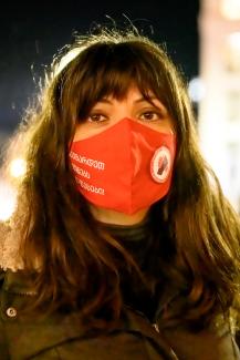 La foto muestra a Sopo Japaridze, uno de los cofundadores de Union Solidarity Network. Sopo tiene cabello castaño largo, con flequillo, ojos marrones y usa una máscara roja del Sindicato de la Red de Solidaridad. La foto está tomada de noche.