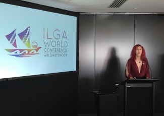 Photo of Sabrina Sanchez speaking next to a screen on Ilga World meeting