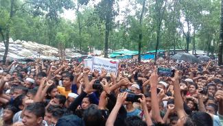 Photo by Rohingya Young civil rights defender Murshid khan showing a crowd mid-protest. Near the center of the image someone is holding up a sign that says "Genocide - Never again"