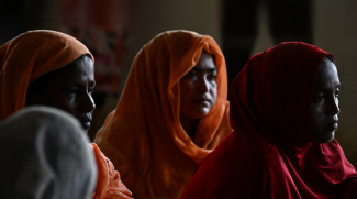 The photo shows 3 Rohingya refugee women wearing orange and red hijabs looking to the United Nations High Commissioner for Refugees delegations (not pictured). The photo was taken during a meeting at a temporary shelter at a government building in Banda Aceh, Aceh. (Credits: AFP/Chaideer Mahyuddin)